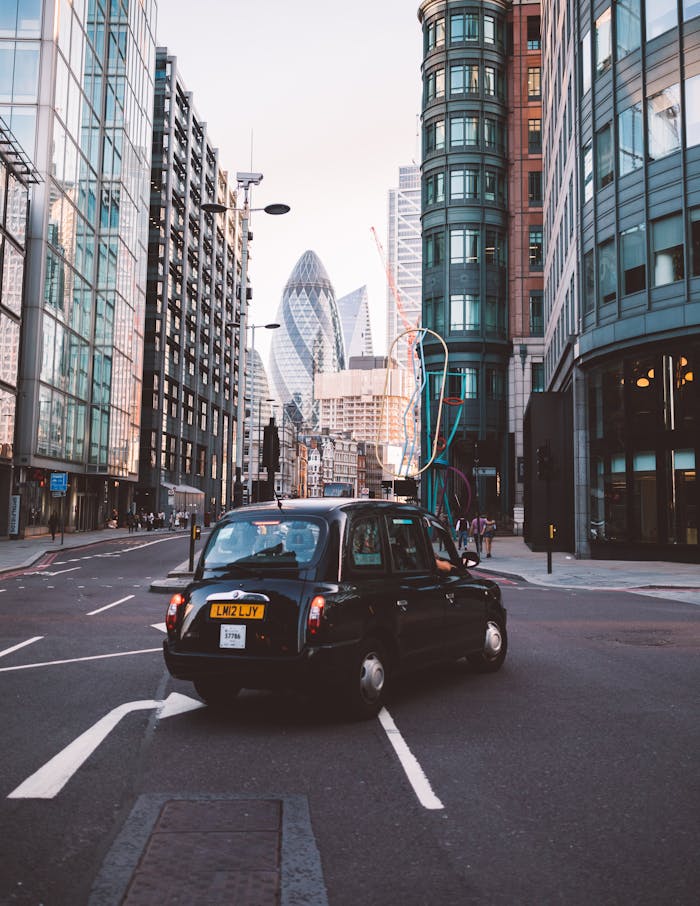 services-03 Classic black taxi navigating the streets of London with iconic skyscrapers in the background.