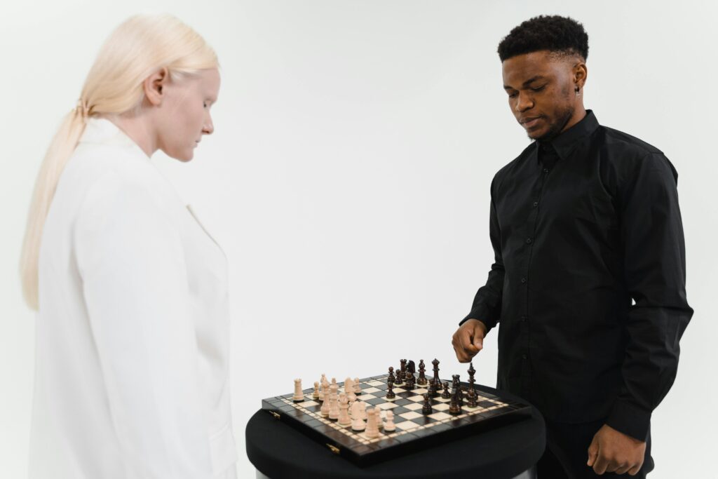 Two adults in contrasting attire playing chess, showcasing strategy and concentration indoors.
